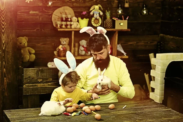 Easter family with fake bunny ears. Father and kid painting Easter eggs.