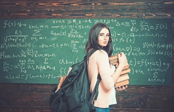 Young female standing in the middle of classroom with huge pile of books in her hand. Beautiful brunette student cramming for exams — Stock Photo, Image