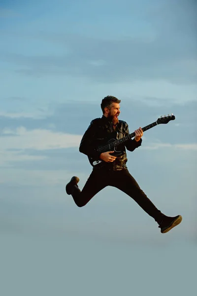 Music is so much fun. Bearded man jump with guitar on blue sky. Hipster guitarist with beard on excited face play in clouds. Like rock star. Feeling free and happy. I love my guitar — Stock Photo, Image