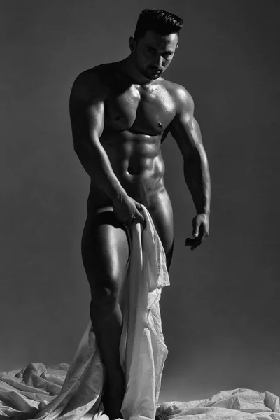 英俊的裸体男子或肌肉健美的健美男子 男子气概 有性感的肌肉躯干 有六个包和腹肌 三头肌 二头肌 皮肤油腻 灰色背景的白色床单 — 图库照片
