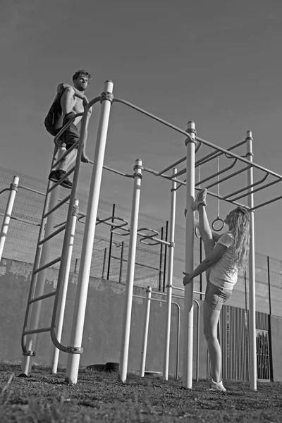 Sportman en Sportvrouw van monkey bars. Sport paar opleiding in metalen jungle gym. Man atleet klimmen op boven- en vrouw split been. Sport training en pilates concept — Stockfoto