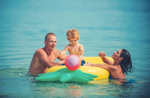 夏休み、海への旅行。父と息子と母は、水でボールをプレーします。パイナップル インフレータブルまたはエアコンのマットレス。モルディブまたはマイアミ ビーチ活動の喜び。カリブの海に幸せな家族カップル — ストック写真