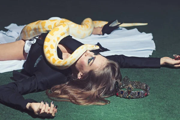 Python se arrastra sobre una mujer con el pelo largo. Mujer sensual con serpiente. Mujer con rostro de maquillaje y serpiente. Modelo de belleza en corona de joyería. Concepto de peligro y miedo — Foto de Stock