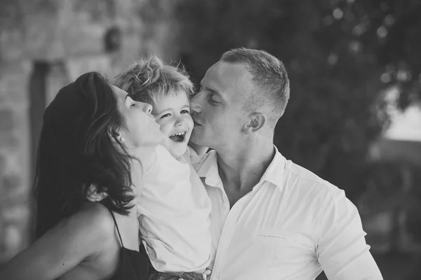 Familia feliz pasar tiempo juntos, fondo urbano. Padres besando a hijo en mejillas, niño feliz con la cara sonriente. Madre y padre aman a su hijo. Concepto familiar feliz. paternidad, abrazos, amor, beso . — Foto de Stock