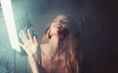 Moda güzellik ve aşk. Kalp şeklinde pencere camına yağmur damlaları. Kız makyaj ile daha önce su ile pencere bırakır. Su ile plastik levha arkasındaki seksi kadın bırakır. Duş ve hijyen kaplıca tedavisi