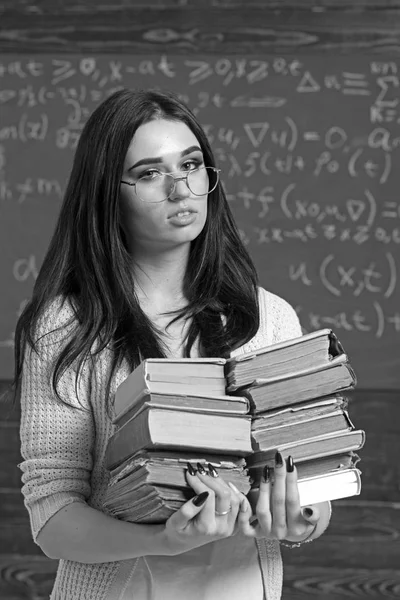 Beautiful brunette girl holding heap of books in her hands. Smart student preparing for exams