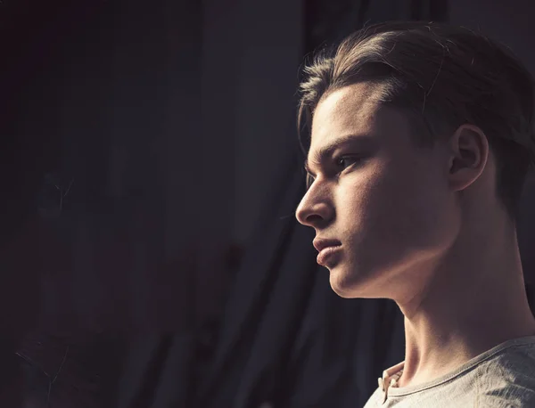 Mann mit selbstbewusstem Gesicht in hellem Hemd, schwarzem Hintergrund. Macho mit stylischem Langhaarschnitt, Seitenansicht. Männlichkeitskonzept. Mann mit glatter Haut und Schatten im Gesicht, Kopierraum — Stockfoto