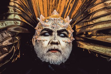 Adam dikenler veya siğiller ile yüz pırıltılar ile kaplı. Şeytan siyah zemin üzerine altın yakalı. Fantezi kavramı. Beyaz sakallı komuta sizde canavar gibi giyinmiş. Uzaylı, iblis, büyücü makyaj.