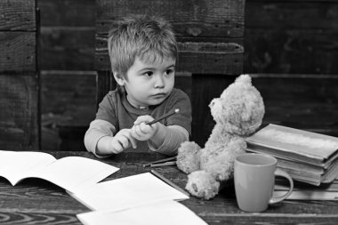 Okuldaki meşgul çocuk. Küçük çocuk copybooks ile tahta masada oturuyor. Sarışın çocuk onun oyuncak ayı arıyorsunuz