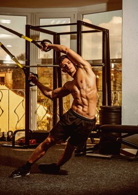 Spor ve spor salonu konsept. Adam çıplak ile gövde ve jimnastik salonu kas göğüs eğitim, trx tadını çıkarın. Sporcu, atlet, kas maço mu egzersiz trx döngüler ile arka plan üstünde pencere.