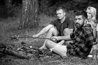 Adam kızarmış sosis arkadaşlarınızla sakallı. Kadın ve erkek piknik, ormandaki şenlik ateşi var. İnsanlar yemek yanıyor. Sevgililer yaz kamp keyfini çıkarın. Yemek yiyecek ve tatil seyahat