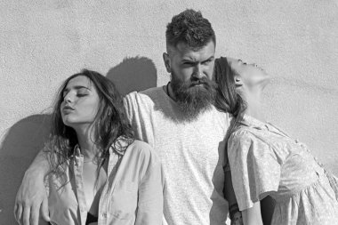 Sakallı adam sıcak güneşli günde iki Bayan sarılmak. Üçlü ısı yaz gününde, arka duvarda uğrar. Adam onları hugs iken kızlar ters tarafı için döndü. Aşk üçgeni kavramı.