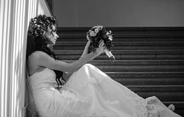 Bride in fashion white dress. Sensual woman with wedding bouquet. Woman with flowers sit on staircase. Girl with bridal makeup and hairstyle. Wedding and waiting for future. — Stock Photo, Image