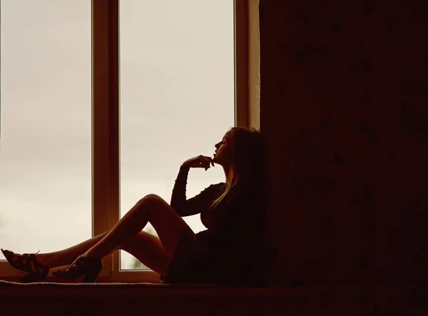 Chica bonita relajarse en el alféizar de la ventana mirando hacia fuera. Mujer relajarse y descansar en casa —  Fotos de Stock