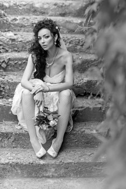 Gelin buketi ile beyaz elbiseli merdivenlerde oturur