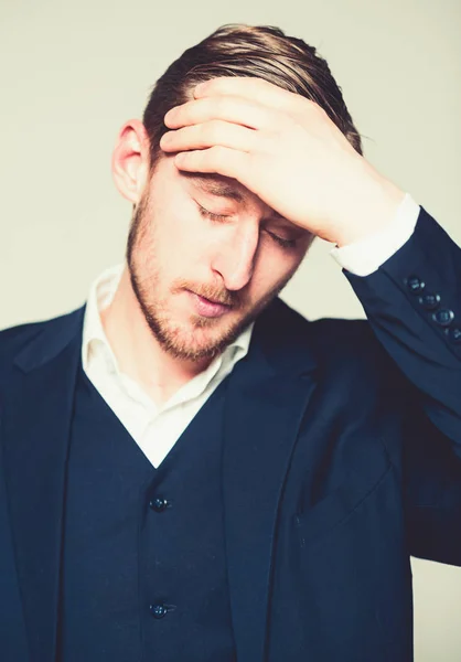 Tired guy with stylish beard and mustache standing with hand on his forehead. Portrait of a young businessman under stress isolated on gray background