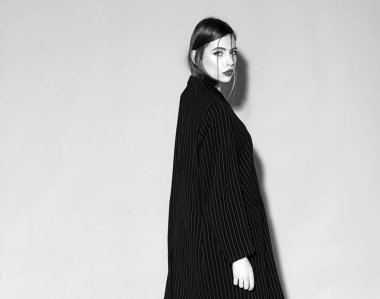 Moda kavramı. Uzun, siyah ceket, gri arka planda katı emin yüz kız. Bayan kırmızı dudaklı kameraya, kopya alanı arıyor. Kadın şık makyaj ve saç modeli ile.