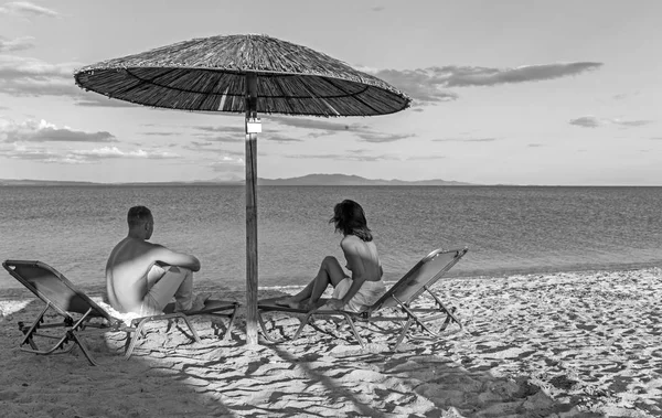 Tropikal kumlu bir plaj şemsiyesi altında oturan genç Çift. — Stok fotoğraf
