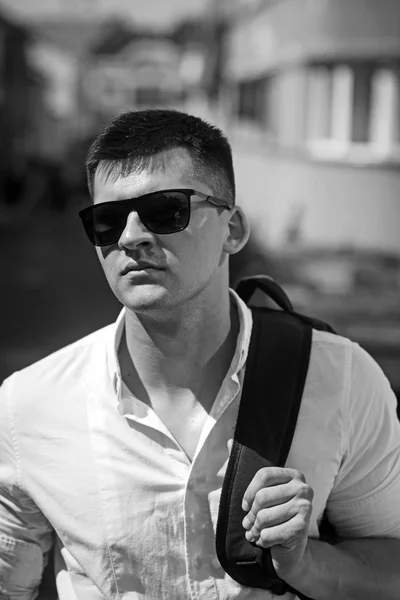 Гарний стильний білий чоловік у модних сонцезахисних окулярах позує на вуличному тлі з рюкзаком на плечах. Мандрівник у місті. Стиль життя міська концепція — стокове фото