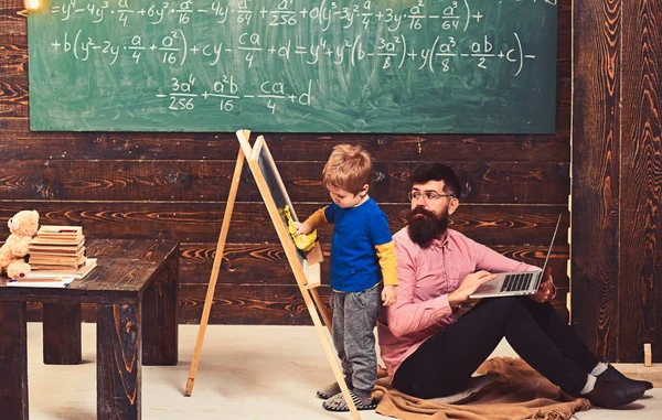 Leraar kid afvegen schoolbord kijken. Kant weergave jongen en de man zit op de vloer met de laptop. Informeel onderwijs concept — Stockfoto