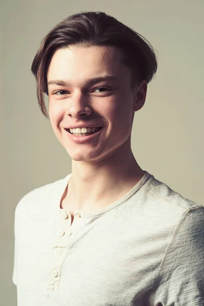 Guy on smiling happy face in light shirt, grey background. Macho with stylish long haircut. Man with smooth skin on face looking at camera. Barber and hairstyle concept.