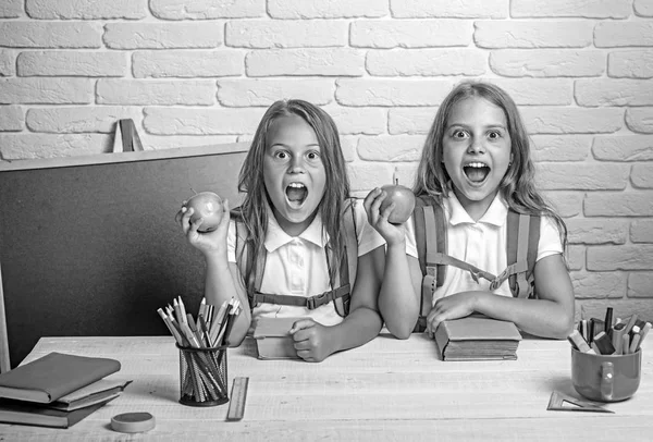 Jovens da escola feliz na aula em 1 de setembro. As meninas comem maçã no intervalo do almoço. Hora da escola das raparigas. Amizade de irmãs pequenas em sala de aula no dia do conhecimento. De volta à escola e à escola doméstica — Fotografia de Stock