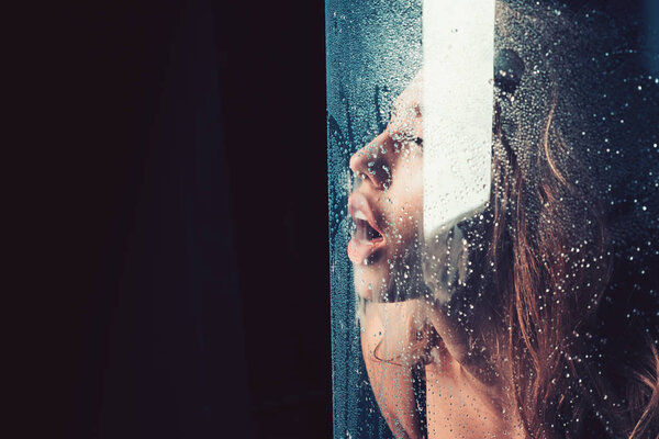 Душ и гигиена курортного лечения. Окно с каплями воды перед девушкой с макияжем. Сексуальная женщина за пластиковым листом с капельками воды. Мода и красота. Капли дождя на стекло с лицом девушки
