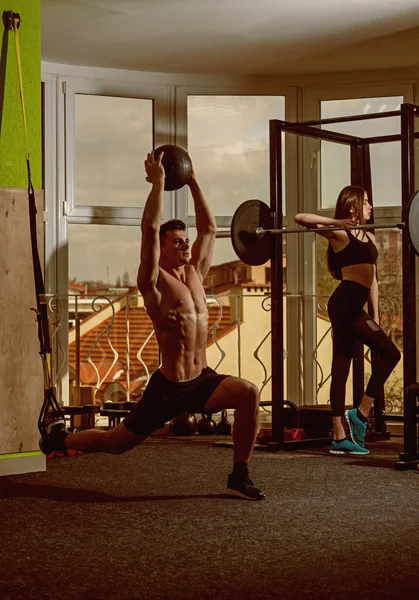 Concepto de deporte y gimnasio. Deportista, atleta, macho muscular hace ejercicio con bucles trx y balón de medicina, chica cerca de la ventana en el fondo. Hombre con el torso desnudo en el gimnasio disfrutar del entrenamiento, trx . — Foto de Stock