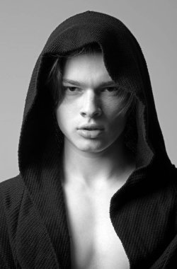 Siyah hood, gri arka planda emin yüz adam. Pürüzsüz cilt yüz, boyun ve göğüs kameraya bakarak üzerinde olan adam. Erkeklik kavramı. Maço siyah bornoz ile kukuleta, yakın çekim.