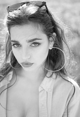 Kadın sakin yüz makyaj, açık renkli, defocused ile. Kız büyük küpeler ve güneş gözlüğü ile açılarak gömlek giyer. Bayan çıplak göğüs ve göğüsler ile çekici görünüyor. Cazibe kavramı.