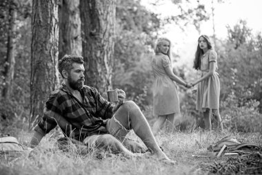 Ormanda kamp arkadaşları. İki kız elele geri çim üzerinde oturan adam bak. Yan görünümü sakallı adam yeşil çayır üzerinde oturan