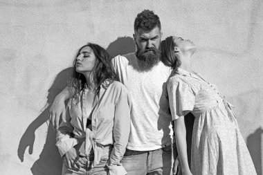 Sakallı adam sıcak güneşli günde iki Bayan sarılmak. Adam onları hugs iken kızlar ters tarafı için döndü. Aşk üçgeni kavramı. Üçlü ısı yaz gününde, arka duvarda uğrar.