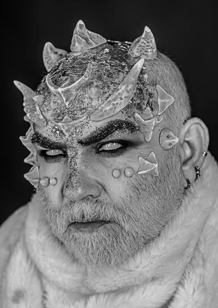 Alien, demon, sorcerer makeup. Demon on black background, close up. Dark arts concept. Senior man with white beard dressed like monster. Man with thorns or warts in fur coat.