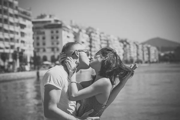 Rakastunut pariskunta suutelemassa meren rannalla. Onnellinen perhe viettää aikaa yhdessä, halata ja suudella, meren ja kaupunkien tausta. Perhelomakonsepti. Miehellä on naisen hiukset, pari kiihkeillä kasvoilla. Rakkauden käsite . — kuvapankkivalokuva