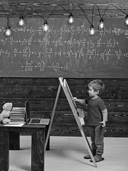Liten pojke skriva på svarta tavlan. Side view kid framför gröna styrelse med matematisk ekvation. Smarta lilla krabaten studera matematik — Stockfoto