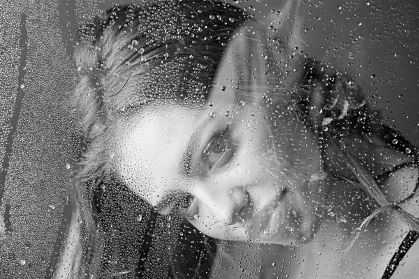 อาบน้ําและทําสปาเพื่อสุขอนามัย ผู้หญิงเซ็กซี่หลังแผ่นพลาสติกที่มีน้ําหยด หน้าต่างที่มีน้ําหยดก่อนที่ผู้หญิงจะแต่งหน้า ฝนตกบนกระจกหน้าต่างด้วยใบหน้าของผู้หญิง แฟชั่นและความงาม — ภาพถ่ายสต็อก