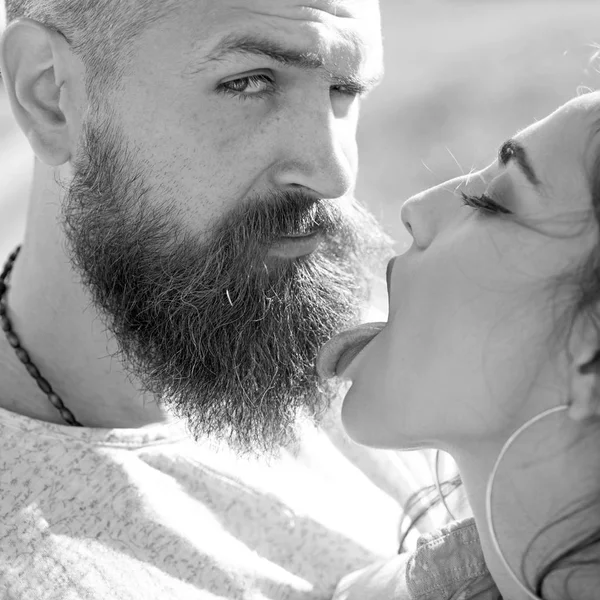 Lady with pink tongue licking bearded macho. Kiss concept. Couple kissing outdoors, nature on background, close up. Couple in love on happy faces relaxing and kissing with tongue.