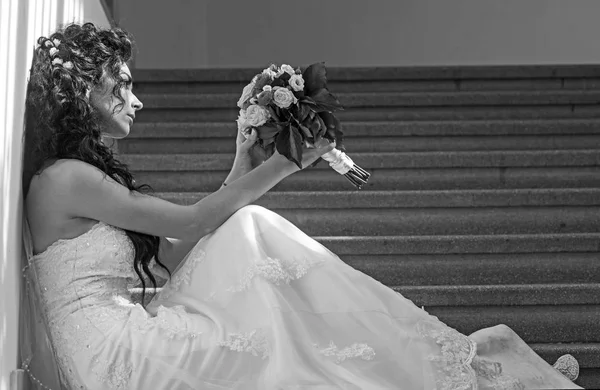 Mulher de moda com buquê de casamento sentar-se na escada. Moda noiva com maquiagem nupcial e penteado em vestido branco com flores — Fotografia de Stock