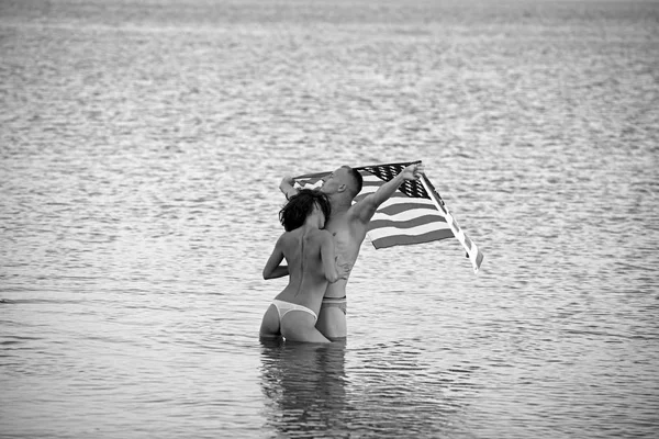 Concept de fête de l'indépendance, vacances de fête de l'indépendance avec couple sexy tenir drapeau américain dans l'eau de mer . — Photo