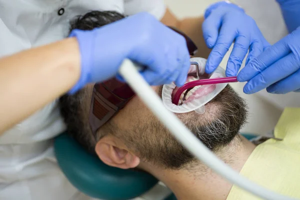 Jeune homme choisissant la couleur des dents chez le dentiste, gros plan. Dentiste féminine vérifiant les dents des patients avec miroir dans la clinique dentaire moderne. Beau homme au cabinet des dentistes . — Photo