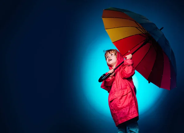 Kinder haben Spaß mit dem Laubfall. Regenende Kinder. fröhlicher Junge im Regenmantel mit buntem Regenschirm. Lustiges Gesicht. Wolken regen Regenschirm. Regenkonzept. Die größten Rabatte für alle Herbstkleidung für Kinder. — Stockfoto