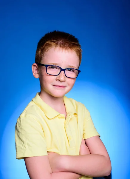 Porträtt av ett litet leende pojke i en roliga glasögon och slips. Tillbaka till skolan. Smart kille använda mikroskopet över blå bakgrund. Kreativ glad god pojke genom Mikroskop medan leende. — Stockfoto