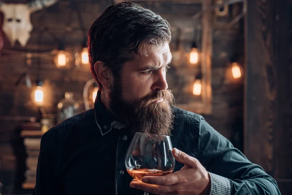 Muž s alkohol pít doma. Vousatý muž sedí u baru. Alkoholik se láhev a sklenice pití koňaku v noci. — Stock fotografie