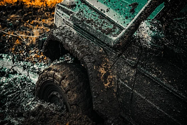 Off-road vehicle goes on the mountain. Bottom view to big offroad car wheel on country road and mountains backdrop. Tracks on a muddy field. Offroad vehicle coming out of a mud hole hazard. — Stock Photo, Image