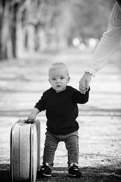 Открытый портрет забавного маленького мальчика, идущего по дороге в сельскую местность, держащего старый чемодан . — стоковое фото
