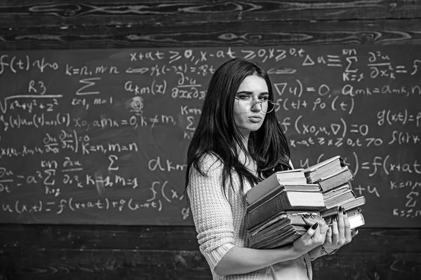 Brunette student wandelen met twee stapels boeken in de voorkant van groen bord vol schrijven. Math undergraduate voorbereiden op examens — Stockfoto