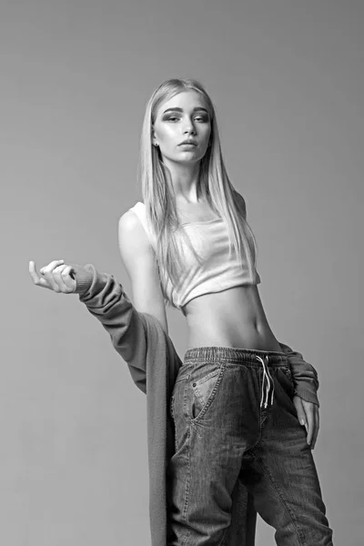 Ragazza bionda con i capelli lisci isolati su sfondo grigio. Giovane modella in jeans posa in studio — Foto Stock