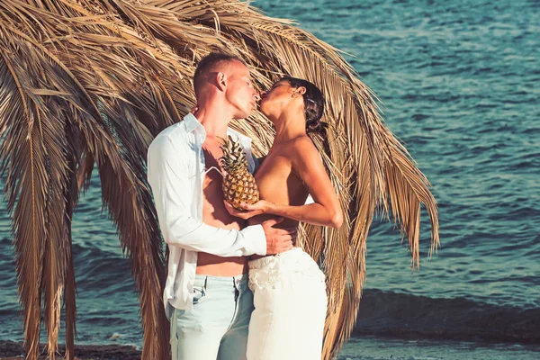 Eingefärbte Vintage-Outdoor-Porträt der schönen romantischen Paar von oben ohne Mädchen und muskulösen Kerl in Jeans küssen mit Ananas am Strand. — Stockfoto