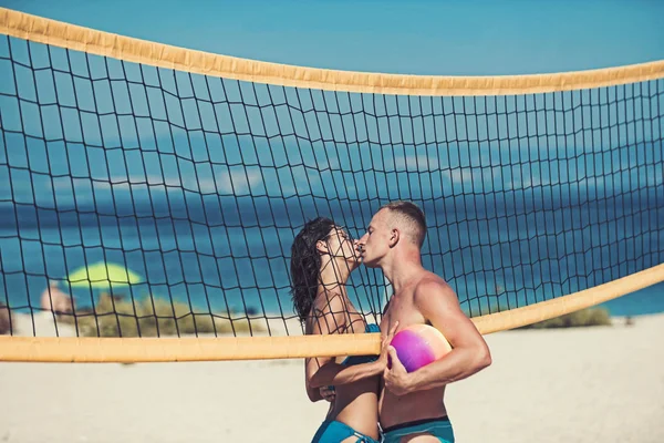 Kärlek och flirta av par. Sexig kvinna och muskulös man med boll på netto. Sommarsemester och resa på semester i Miami. Par i kärlek spela volleyboll på sunny beach. Sportaktivitet och hälsa — Stockfoto