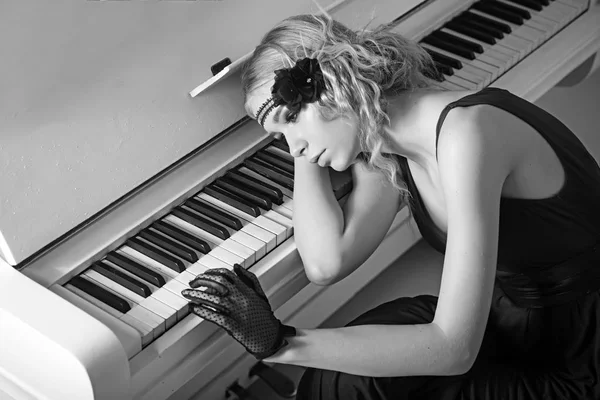 Young actress lying on piano overwhelmed with memories. Sad blond girl leaning on keyboard. Roaring twenties fashion concept — Stock Photo, Image